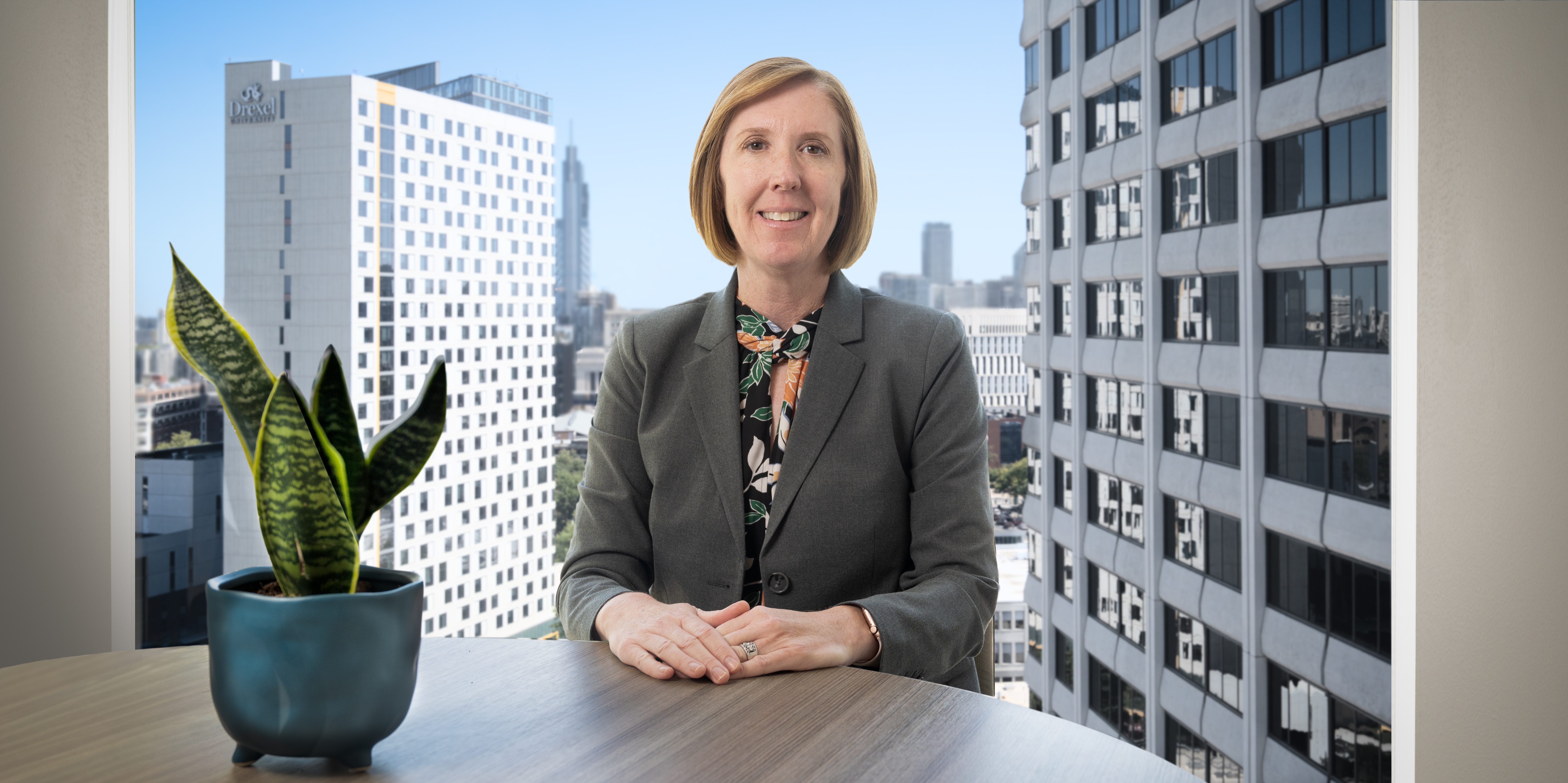 Dean Emily Roper, PhD, sitting a table with city scape behind her